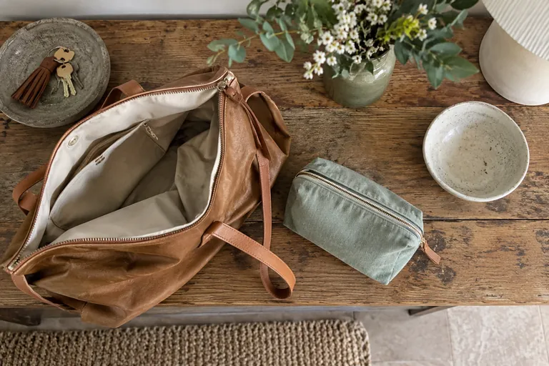 Un sac ouvert, une trousse fermée et une coupelle vide sont posés sur un meuble.