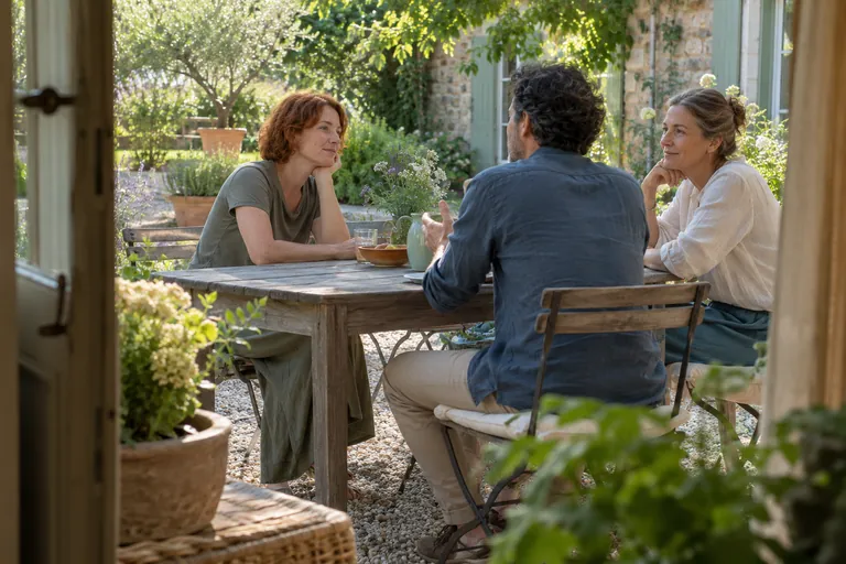 Trois adultes discutent autour d’une table dans un jardin