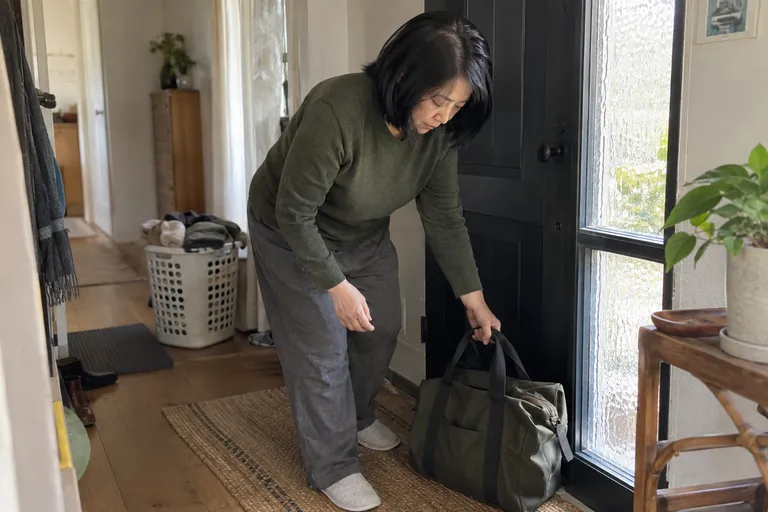 Une femme pose son sac près de la porte, un panier de linge en arrière-plan.