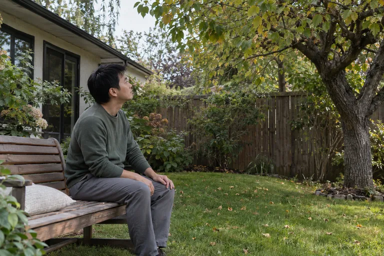 Un homme assis sur un banc regarde un arbre dans un jardin.
