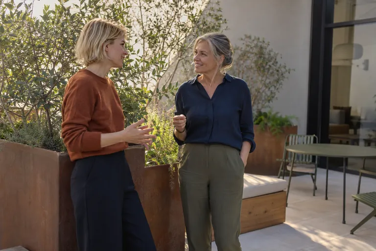Deux femmes discutent debout sur une terrasse.