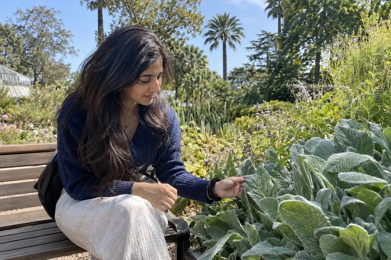 Une jeune femme dans un jardin touche la texture d’une feuille, attentive au moment présent