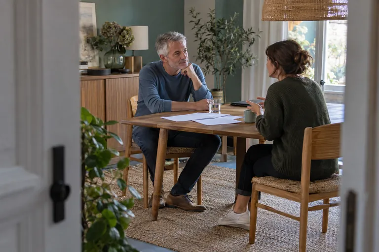 Deux adultes discutent à une table avec des feuilles posées devant eux